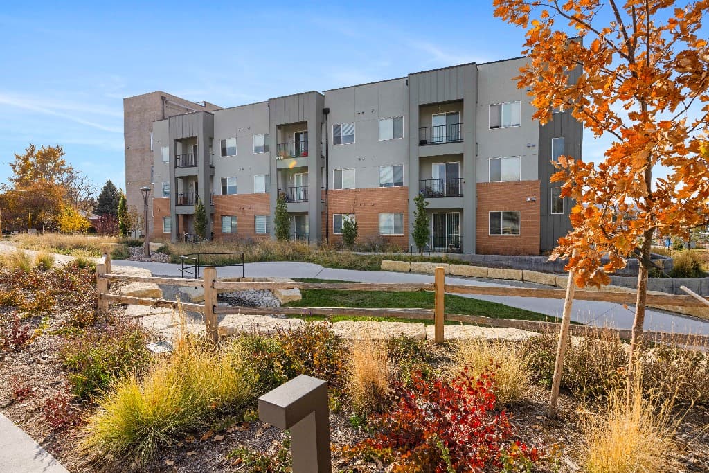 Arvada Apartments, a three-story building with balconies and native landscaping in autumn