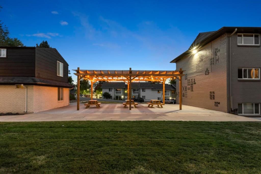 Midtown Plaza courtyard at dusk with a lit pergola and picnic tables between two apartment buildings